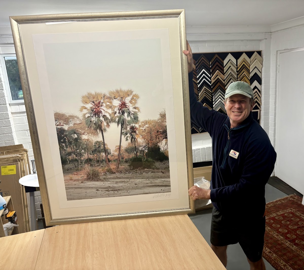 Brenton Nicholls holding a large framed Palm Trees print by Caroline Gibello — Framehouse, Brookfield